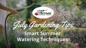 Person watering flowers in a summer garden with a hose and spray nozzle, with text ‘July Gardening Tips: Smart Summer Watering Techniques’ for Thomas Greenhouse & Gardens.