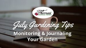 Open garden journal with a coffee mug on a wooden table, featuring text ‘July Gardening Tips: Monitoring & Journaling Your Garden’ for Thomas Greenhouse & Gardens.